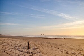 Ein Strand mit blauem Himmel, sandigem Ufer und einer entfernten Felsformation im Hintergrund.