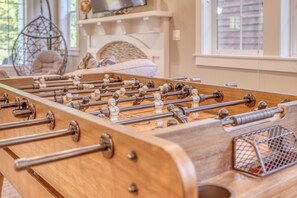 A wooden foosball table with metal rods and figure tops, set in a room with a bed and a hanging chair in the background. - Family & Dog friendly Nedonna Beach Home, Hot Tub, BBQ, Short Walk to the Beach (Rockaway Beach)