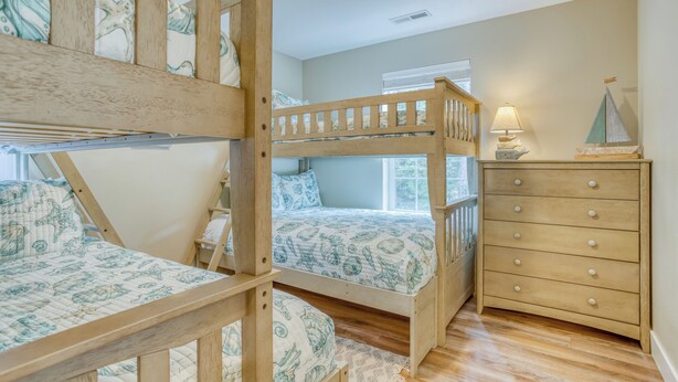 Une chambre avec un lit superposé, une échelle en bois, une commode avec des tiroirs et une lampe posée sur la commode.