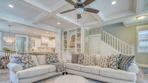 Un salon comprenant un canapé d’angle, un ventilateur de plafond, des étagères intégrées et un escalier.