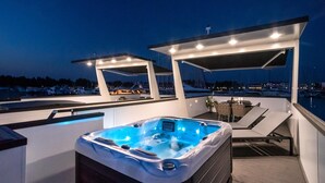 Een jacuzzi op een terras, uitzicht op boten en een jachthaven in de schemering.