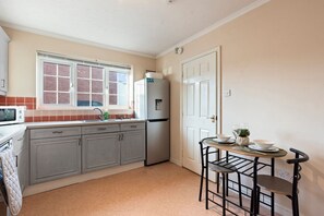 A compact kitchen with a refrigerator, sink, and a dining area with a table and chairs. - Applin House|5BR Contractor Stay|Parking WiFi (Bristol)
