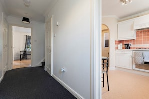 Ein Flur, der in einen Essbereich mit Tisch und Stühlen sowie in eine Küche mit Schränken und einer gefliesten Spritzwand führt. Eine Tür öffnet sich zu einem weiteren Raum.