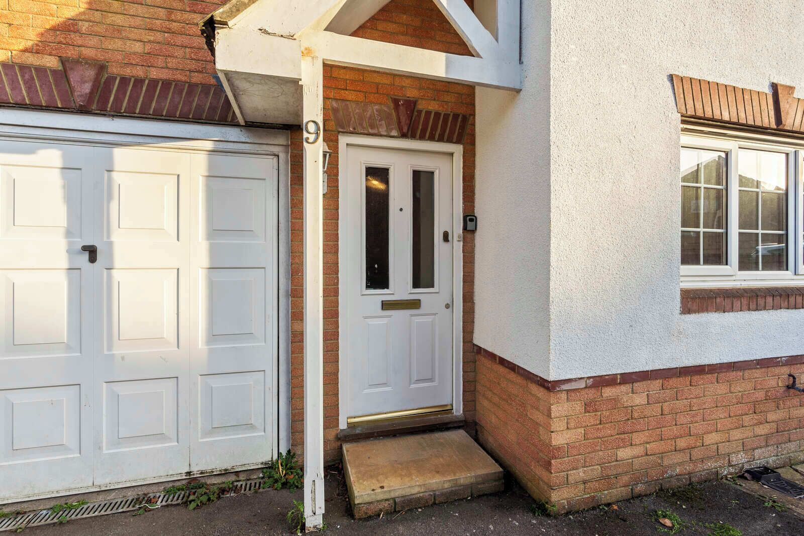 A residential property with a white garage door, a front door with a small step, and a window with a white frame.
