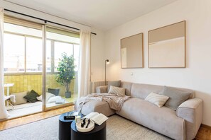 A modern living room with a sofa, a coffee table, a potted plant, and a sliding glass door leading to a balcony. - A light-filled one-bedroom in Cuatro Caminos, where a private sixth-floor balcony looks out over open sky, a quiet place for morning coffee a short walk from the Bernabéu. (MADRID)