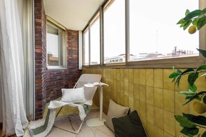 A corner room with a brick wall, a window, a chair, a small table, and a plant. - A light-filled one-bedroom in Cuatro Caminos, where a private sixth-floor balcony looks out over open sky, a quiet place for morning coffee a short walk from the Bernabéu. (MADRID)