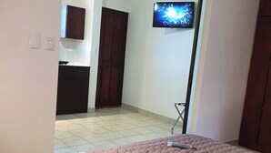 A hotel room with a bed, a television on the wall, a ceiling fan, and a view of the adjacent room. - Marina Loft #103, 1 Floor (Sardinal)