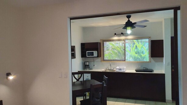 A compact kitchen with a dining area, a ceiling fan, and a window with blinds. - Marina Loft #103, 1 Floor (Sardinal)