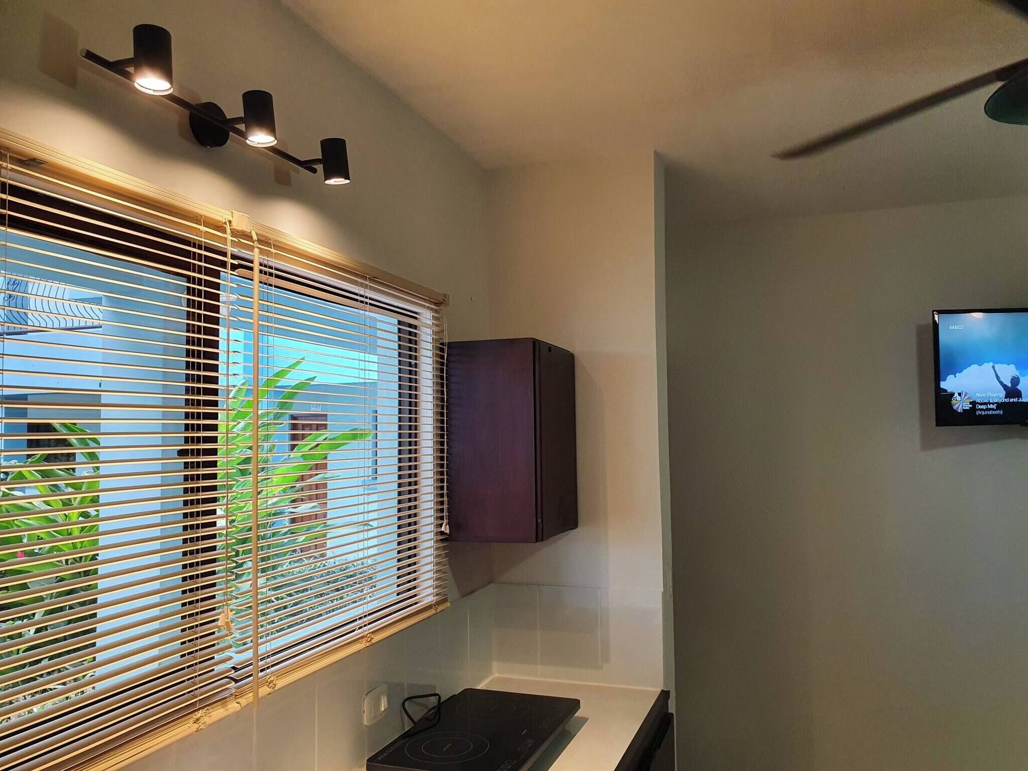 A room with a window with horizontal blinds, a wall-mounted cabinet, and a flat-screen TV on the wall.