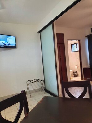 Ein Zimmer mit an der Wand montiertem Fernseher, einer Projektionsleinwand, einem kleinen Tisch und einem Stuhl.