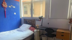 A bedroom with a single bed, a desk with a chair, a window, and a wall with a decorative item. - Spacious 170 m² Loft – 3 Bedrooms – Canal St-Martin – Fully Furnished & Designer (Paris)