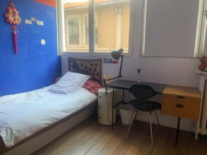 Ein Schlafzimmer mit einem Einzelbett, einem Schreibtisch mit Stuhl, einem Fenster und einer Wand mit einer Dekoration.