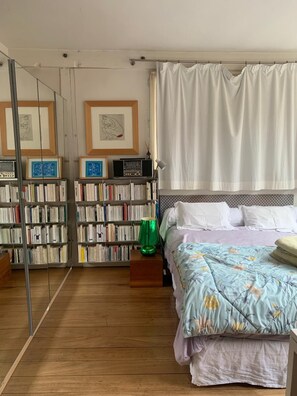 A bedroom with a bed, a bookshelf, a mirror, and a window with curtains. - Spacious 170 m² Loft – 3 Bedrooms – Canal St-Martin – Fully Furnished & Designer (Paris)