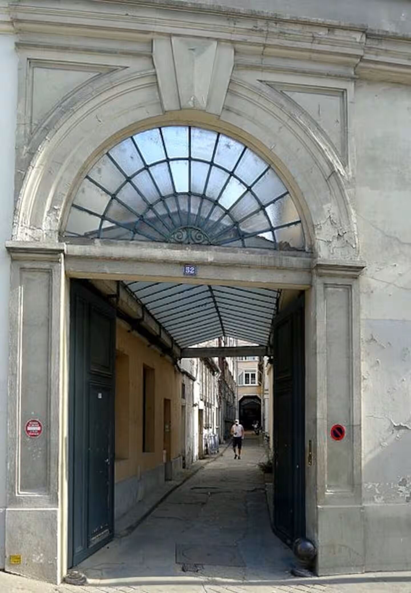 An arched passageway with a glass roof, leading to a building entrance.