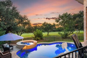 A swimming pool with a hot tub, surrounded by a brick patio, outdoor furniture, and a view of a golf course at sunset. - Luxury 5BR on Golf Course: Pool, Hot Tub, EV Charger (Round Rock)
