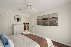 Een slaapkamer met een bed, een kaptafel, een spiegel, een plafondventilator en een muur met drie ingekaderde foto's.