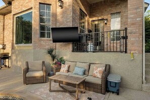 A patio area with a wicker sofa, a wooden coffee table, and a trash bin. - Luxury 5BR on Golf Course: Pool, Hot Tub, EV Charger (Round Rock)