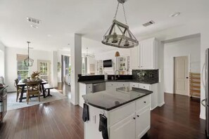 A spacious kitchen with a central island, white cabinetry, and a hanging light fixture. - Luxury 5BR on Golf Course: Pool, Hot Tub, EV Charger (Round Rock)