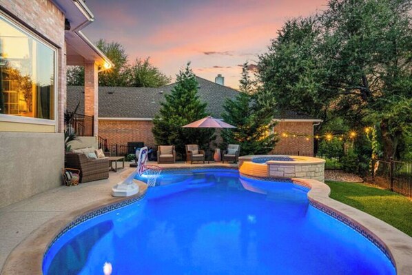 Ein Swimmingpool mit Whirlpool, umgeben von Gartenmöbeln und einer Ziegelmauer.