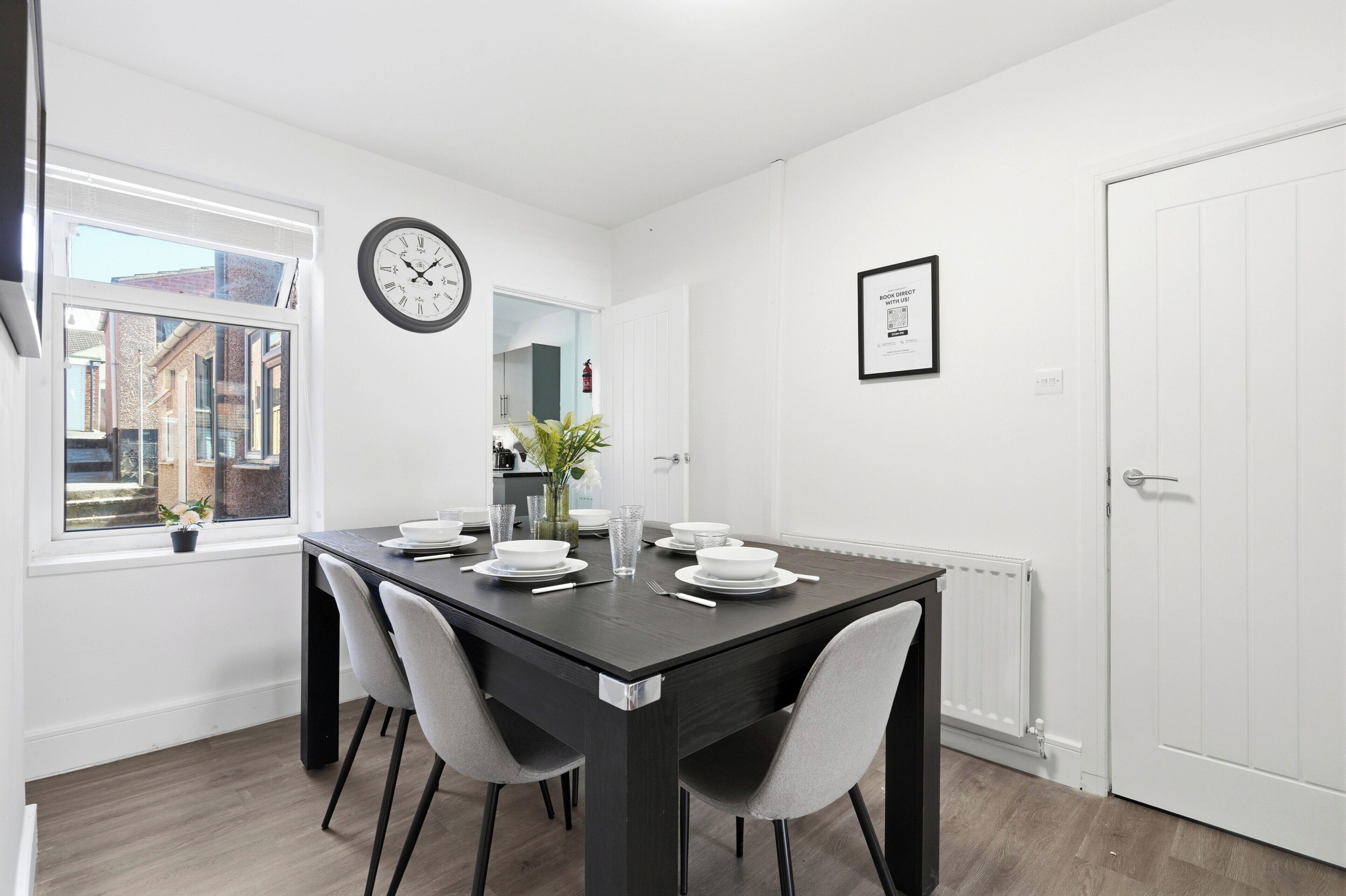 A dining area with a table set for four, a clock on the wall, and a framed picture.
