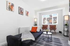A modern living room with a black sofa, two armchairs, a round coffee table, and a large window with blinds. - Spacious Home | Pool Table | Sleeps 8 (CoventrY)