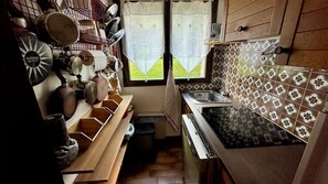 A compact kitchen with a stove, sink, and a window with curtains. - Stay at the heart of the slopes in Megève! (Megève)