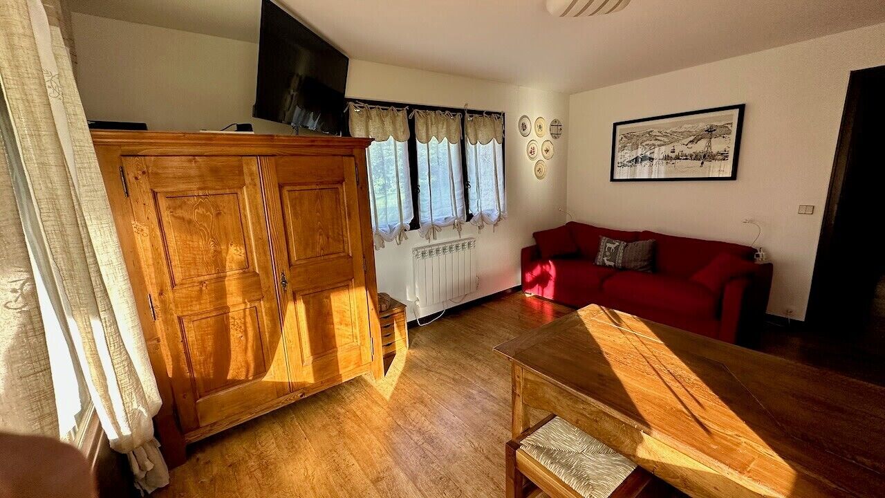 A room with a wooden wardrobe, a red sofa, a wooden table, and a radiator.