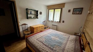 A bedroom with a wooden bed, a dresser, a chair, a radiator, and a window with curtains. - Stay at the heart of the slopes in Megève! (Megève)