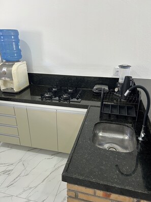 A kitchen with a gas stove, a coffee maker, a water dispenser, and a sink.