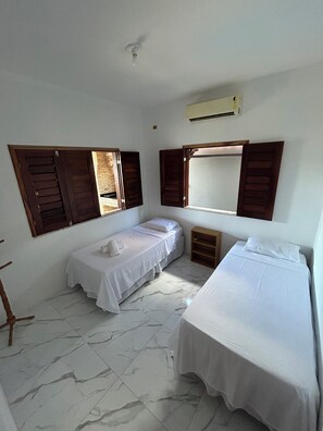 Ein Zimmer mit zwei Betten, einem Holzschrank, einem kleinen Tisch und einem Fenster mit Fensterläden.