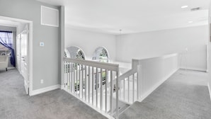 A spacious hallway with a white railing, a door leading to a room with a blue towel, and a window with a view of greenery. - Waterfront Home | Pool, Kayaks, Air Hockey & Foosball (Marco Island)