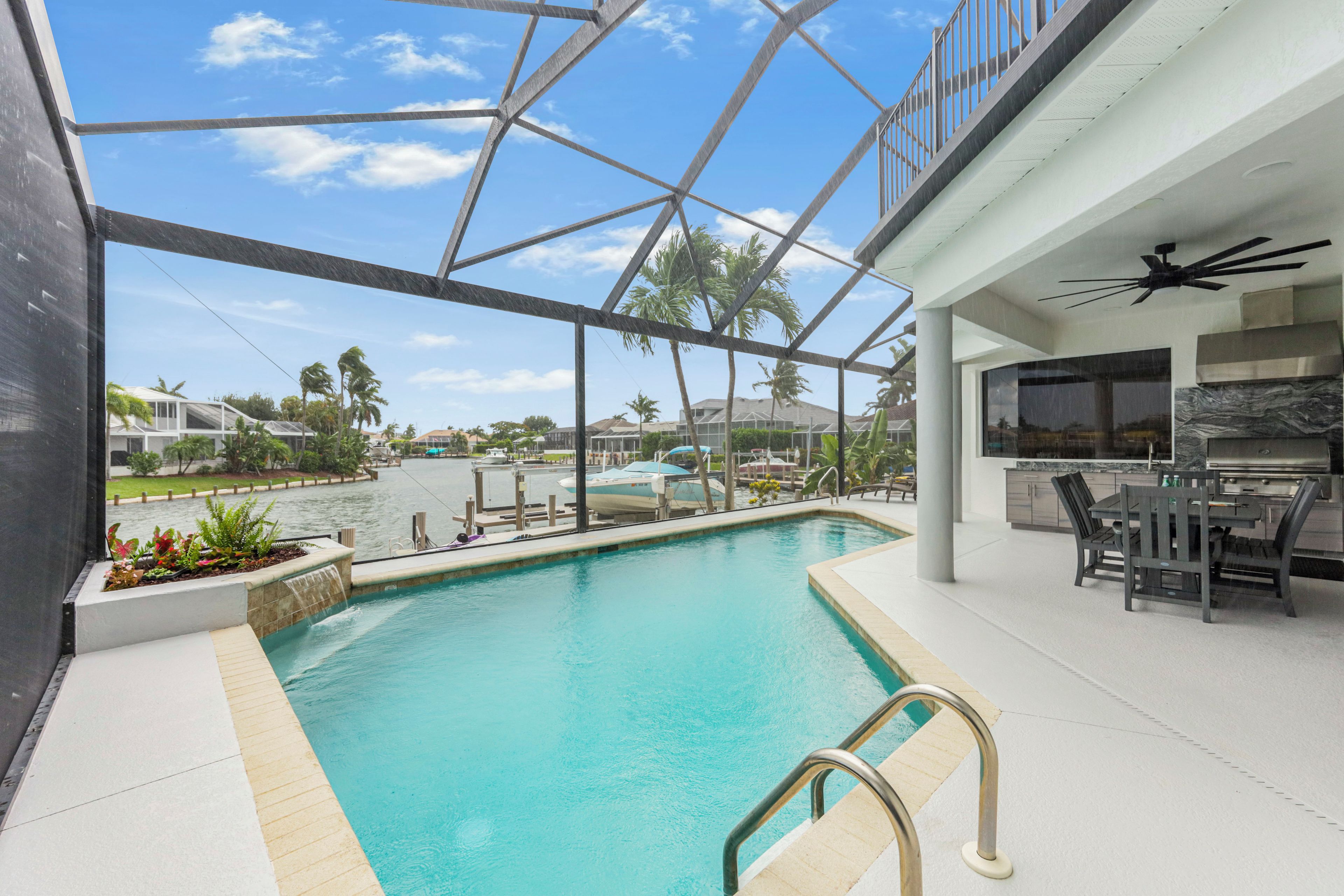 An indoor swimming pool with a view of the surrounding area, including a boat dock and palm trees.