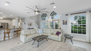 A spacious living area with a large white sofa, a coffee table, and a dining area with chairs. - Waterfront Home | Pool, Kayaks, Air Hockey & Foosball (Marco Island)