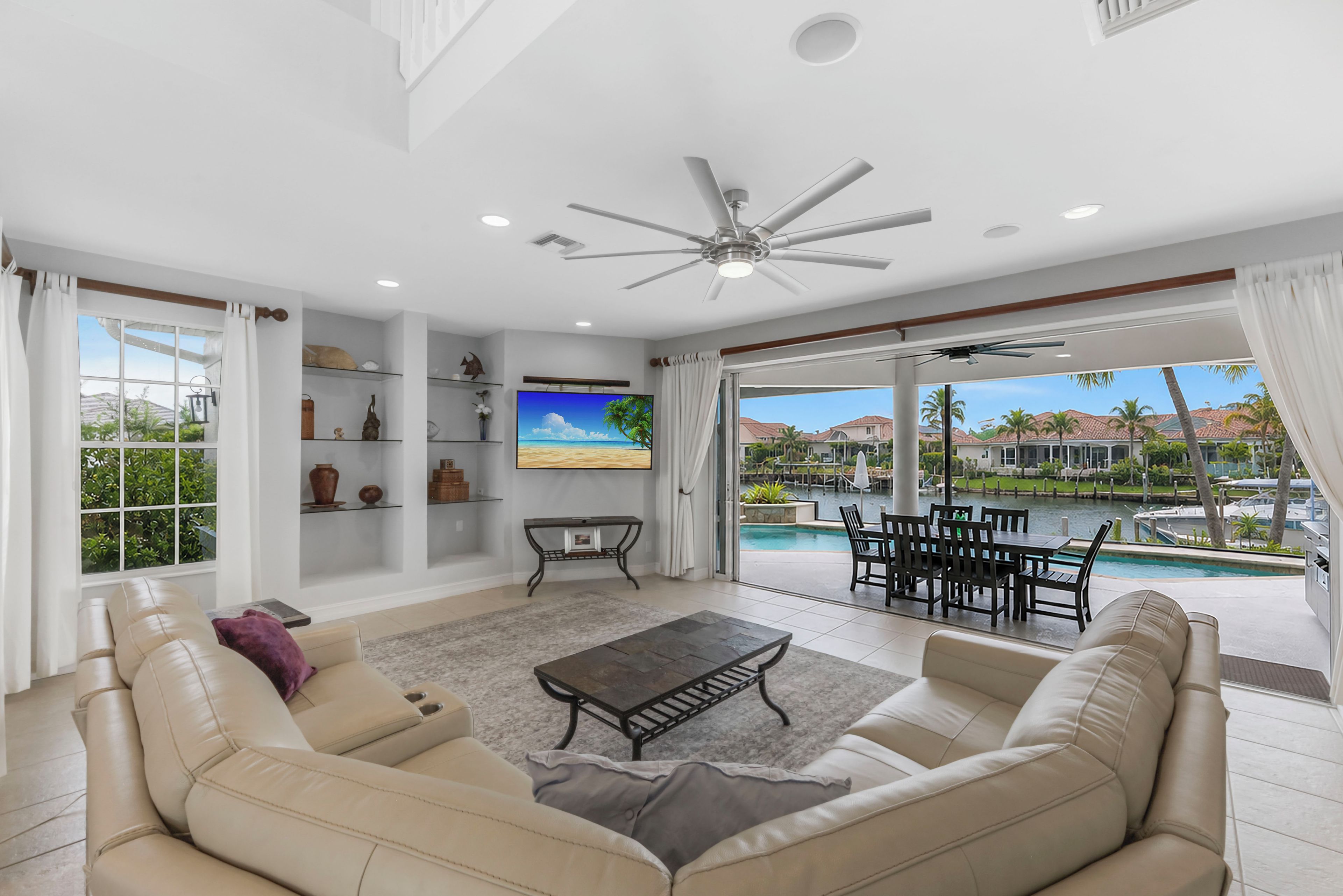 A spacious living room with a sofa, coffee table, and a TV. There is a balcony with a pool view.