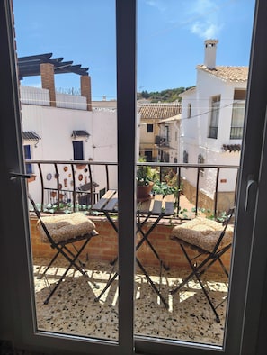 Ein Balkon mit zwei Klappstühlen und einem Blumentopf, der auf einen Innenhof mit einem weißen Gebäude und einem Ziegeldach blickt.