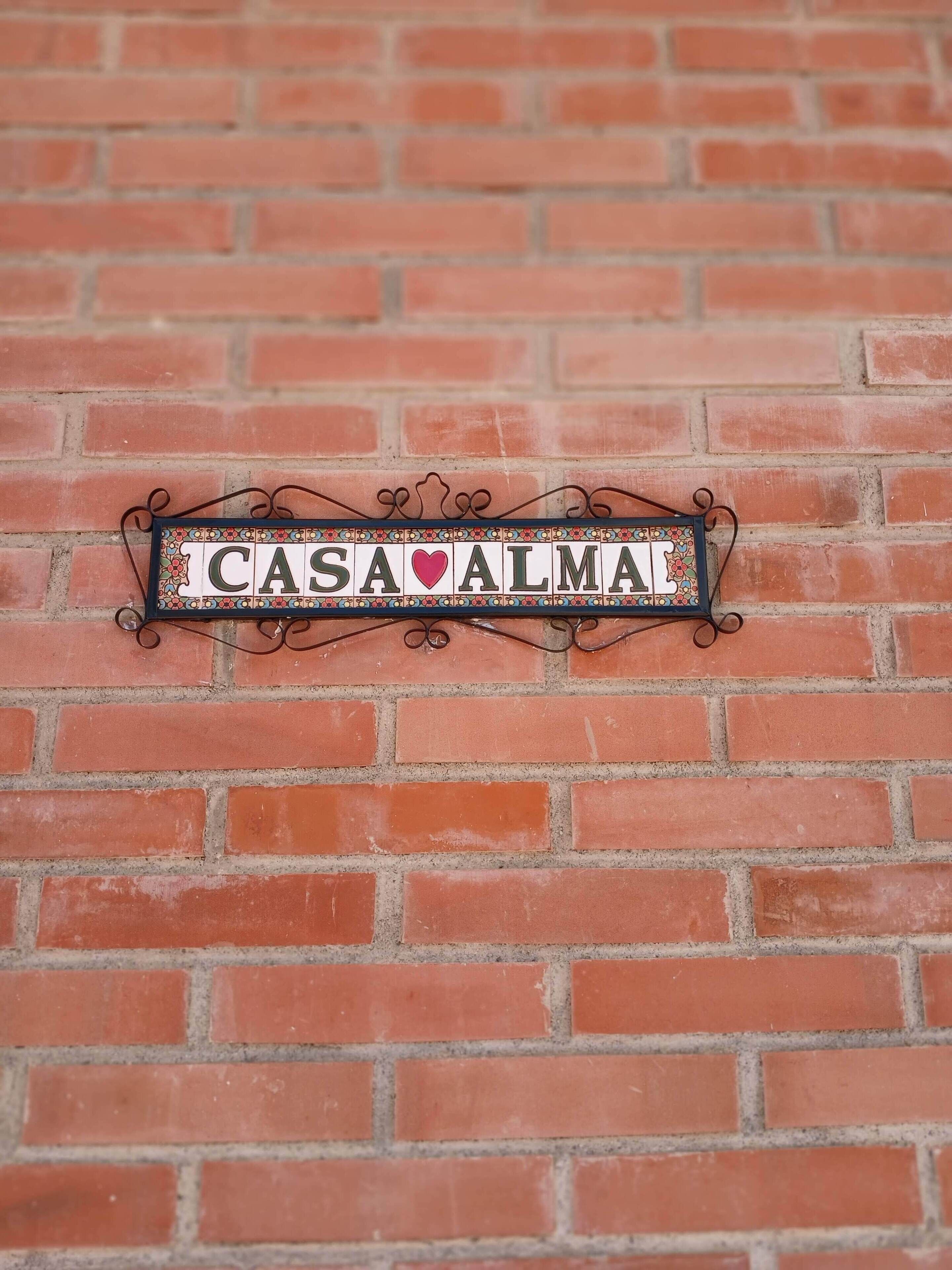 A decorative sign with the text 'CASA ALMA' mounted on a brick wall.