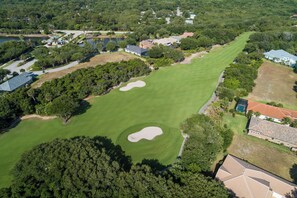 Luftaufnahme eines Golfplatzes mit mehreren Sandbunkern, umgeben von Wohnhäusern und dichter Vegetation.