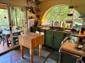 A kitchen with a large window, wooden table, and green cabinets. - Charming Adirondack Retreat Overlooking Lake Luzerne (Lake Luzerne)