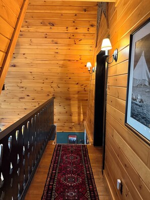 Un intérieur en bois avec un escalier, un tapis à motifs et un tableau encadré au mur.