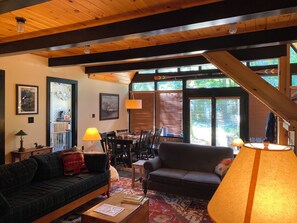 A cozy living room with wooden beams, a dining area, and large windows. - Charming Adirondack Retreat Overlooking Lake Luzerne (Lake Luzerne)