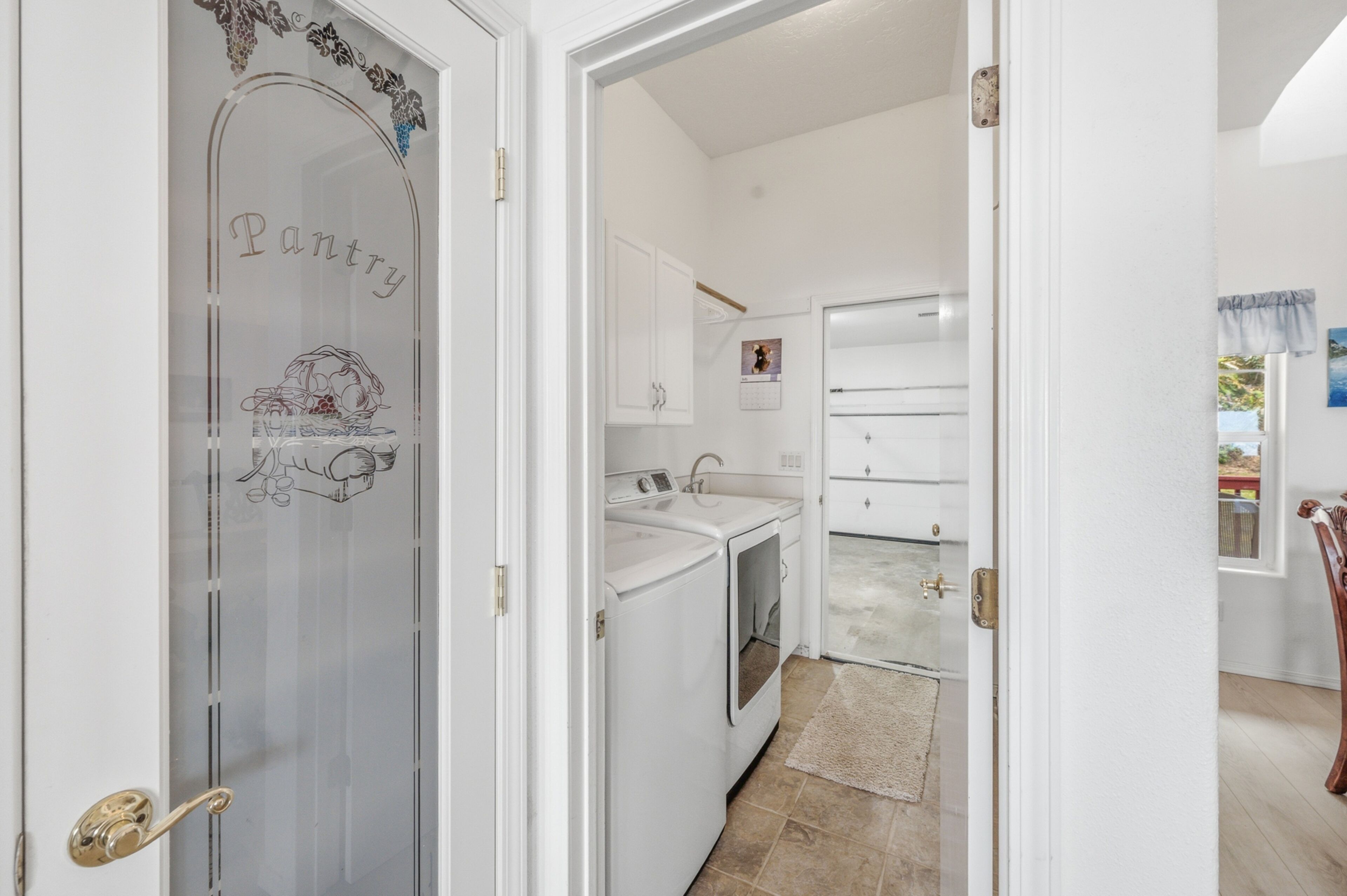 A narrow hallway leading to a kitchen with white appliances and a tiled backsplash.