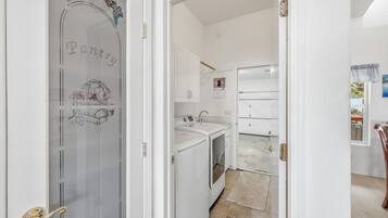 A narrow hallway leading to a kitchen with white appliances and a tiled backsplash.