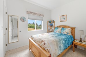 Una camera da letto con un letto di legno, un comodino con una lampada, una finestra vista sul verde e un orologio a muro.
