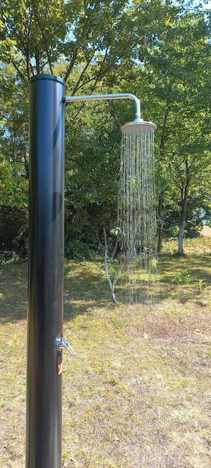 Metallinen vesiaihe, jossa on suihku ja riippuva elementti, ja joka on sijoitettu nurmialueelle, jonka taustalla on puita.
