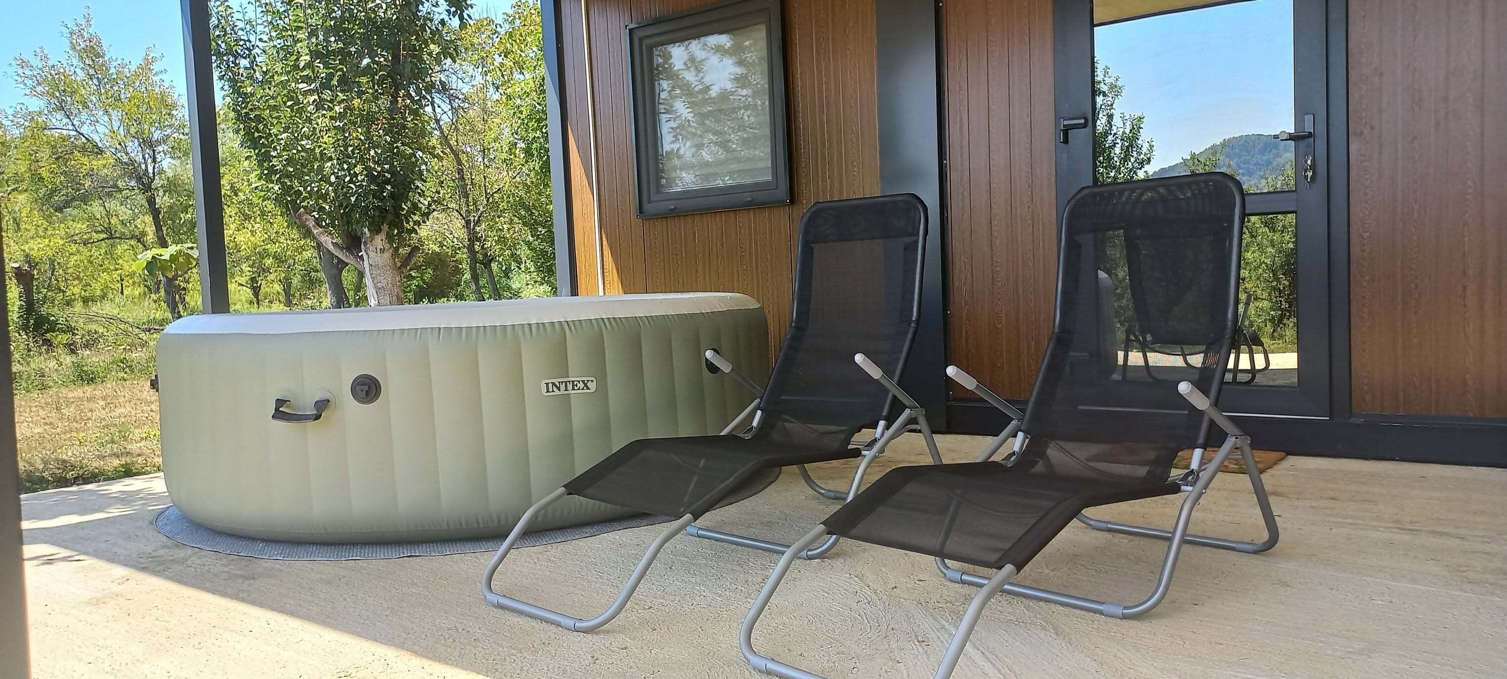 Un jacuzzi y dos sillas reclinables en un patio con revestimiento de madera y ventanas amplias.