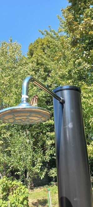 A metal structure with a curved arm and a cylindrical base, set against a backdrop of green foliage.