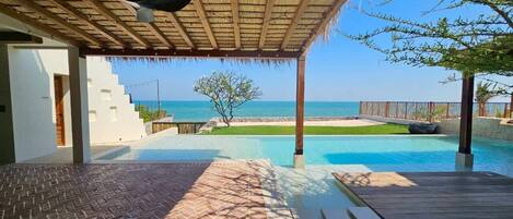A pool area with a view of the sea, a covered patio, and a brick pathway.