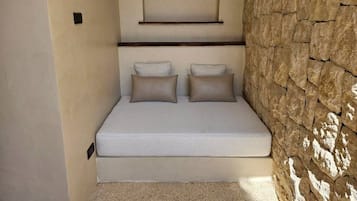 A small, cozy room with a bed, a wall-mounted shelf, and a textured stone wall.