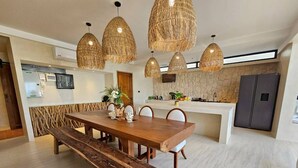 Una cocina moderna con comedor, que cuenta con una mesa de madera, bancos y lámparas colgantes de fibra.
