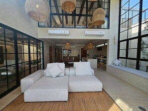 Un salón amplio con un sofá grande, lámparas de techo de mimbre y ventanas grandes.